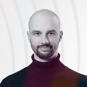 Profesionální portrét Jonáše Čumrika ze společnosti Solvo, plešatý muž s vousy v bordovém roláku na šedém pozadí