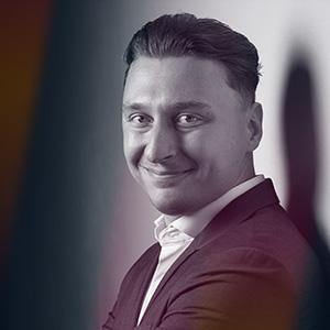 Dominik Buršík, Senior Account Executive CEE & SEU ve společnosti Bloomreach, oblečený v elegantním saku a košili, pózuje na stylizované fotografii s jemnými barevnými přechody a stíny. Dominik vystoupí jako řečník na konferenci Eshopista.