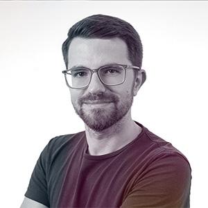 Na fotografii je zachycen sympatický mladý muž s upraveným plnovousem a brýlemi v neformálním burgundsky červeném tričku. Jeho přátelský, sebevědomý úsměv a uvolněný postoj vyzařují profesionalitu i přístupnost zároveň. Portrét je zpracován v moderním stylu s jemným přechodem do tmavšího pozadí, což vytváří příjemnou hloubku snímku. Neformální business styl oblečení perfektně odráží současný trend v technologickém a digitálním sektoru, kde se klade důraz na autenticitu a přirozenost. Fotografie svým zpracováním skvěle vystihuje osobnost člověka, který se pohybuje na pomezí businessu a digitálních technologií.