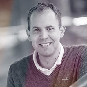 Portrét usmívajícího se muže v šedém svetru s bílým límečkem, který se dívá přímo do kamery. Pozadí je rozostřené a působí profesionálním dojmem. Na fotografii je Jiří Raška, CTO a Co-Founder společnosti Partners Banka.