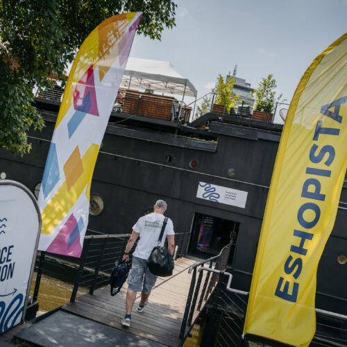 Muž s taškami kráčí po můstku na loď mezi prapory „Eshopista“ a „Recepce“.