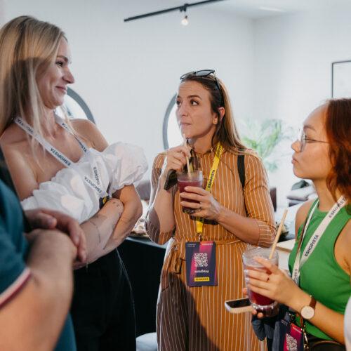 Skupina s lanyardem „ESHOPISTA“ konverzuje a pije červené smoothie při neformálním networkingu.
